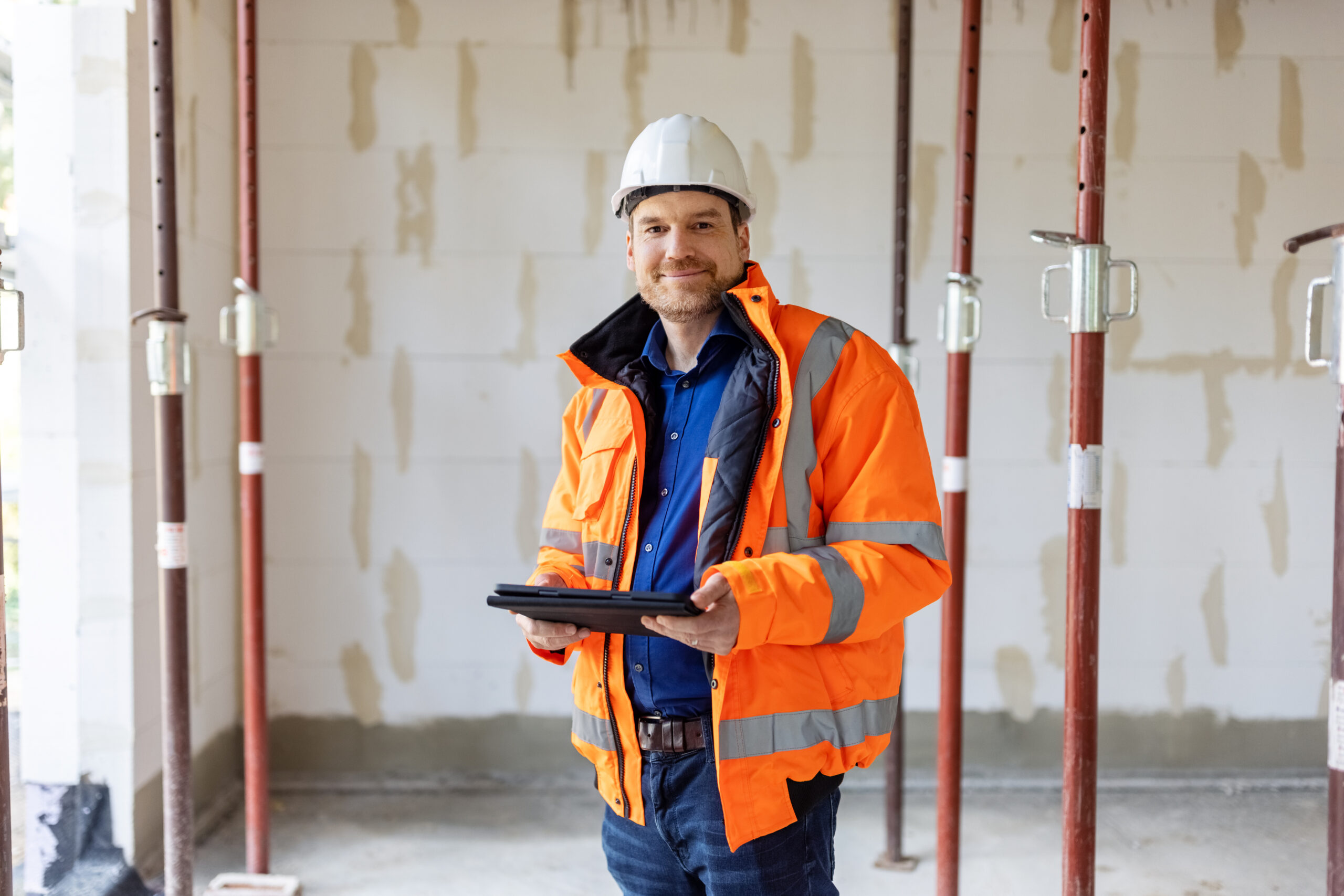 Mann med oransje vest, hvit hjelm og ipad, ser i kameraet.